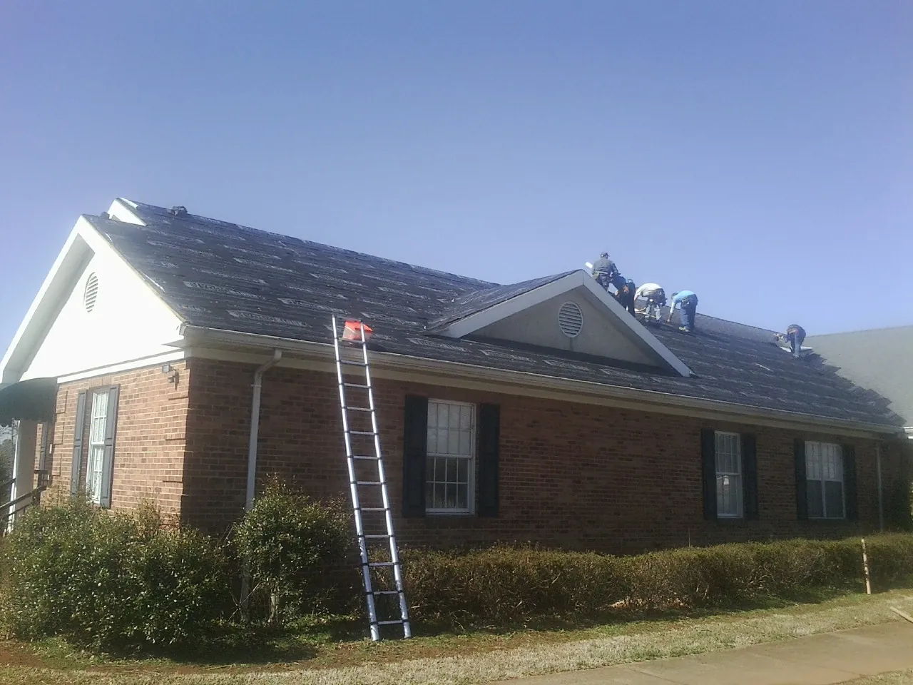 Crew tearing shingles off a brick ranch roof with a ladder set — Metal Roof Repair work by our crew in Faxon