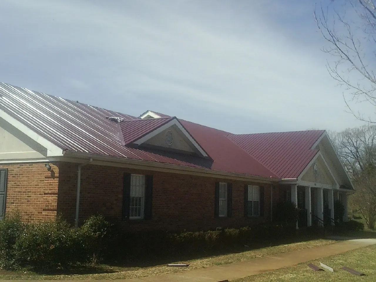 Red metal roof with gabled entries on a long brick building, from a Hail Damage Roof Repair job in Faxon