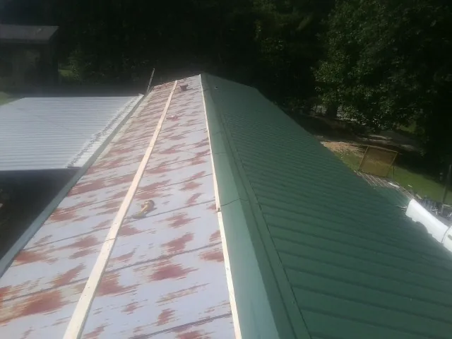 Old rusted panels beside newly installed green metal roofing — Wind Damage Roof Repair by Roofing Brothers in Faxon