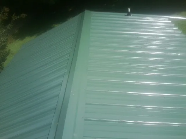New green metal panels meeting at the ridge of a roof — Flat Roof Repair work by our crew in Faxon