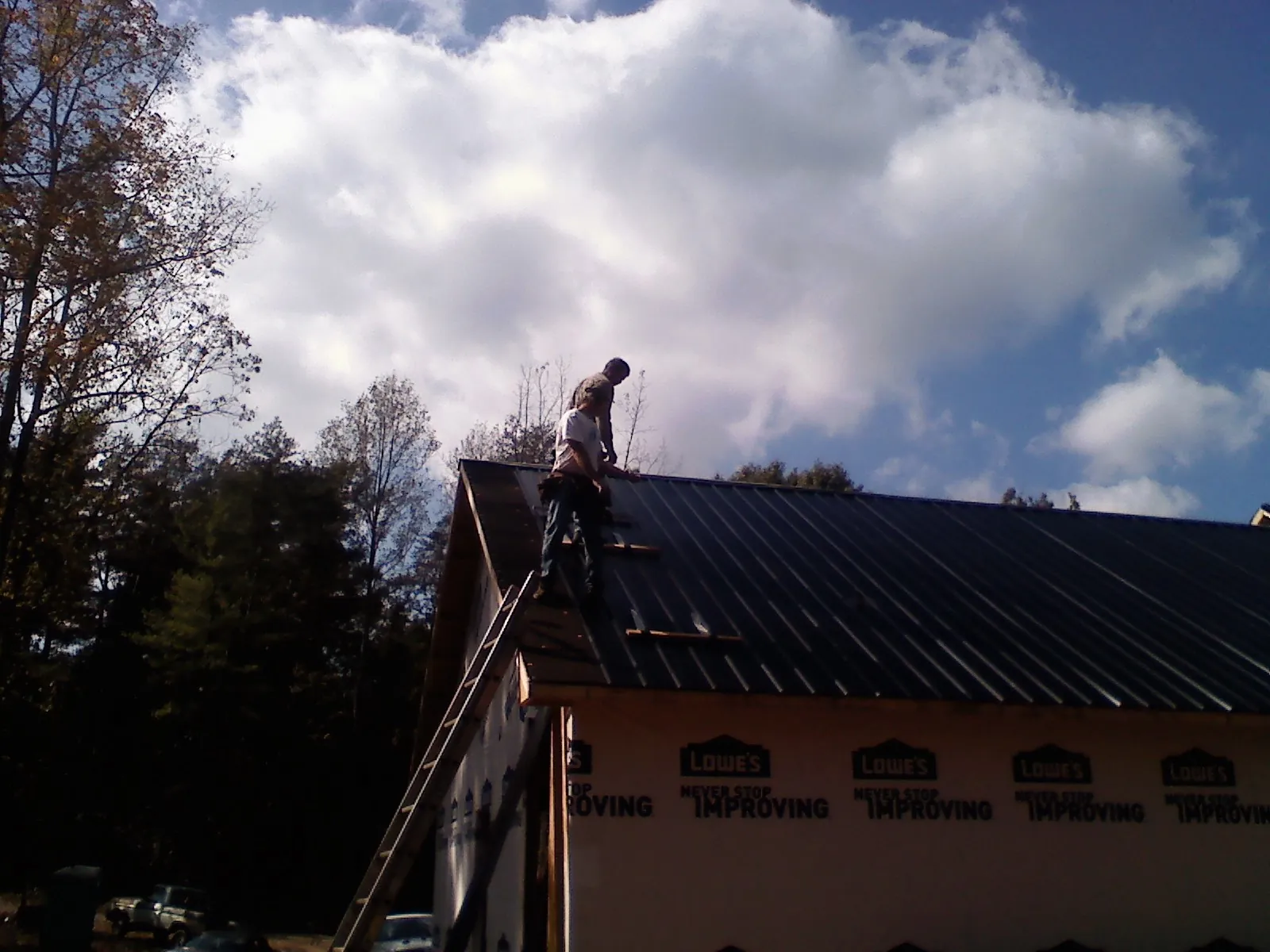 Roofer fastening dark metal panels high against a cloudy sky, from a Roof Inspection job in Faxon