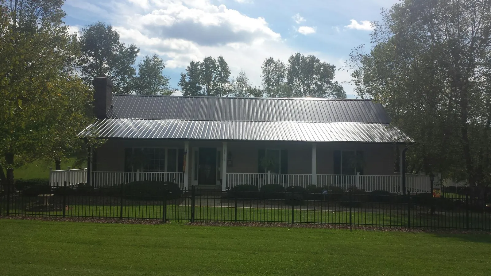 Gray metal roof on a brick ranch with a full width front porch — Gutter Guard Installation work by our crew in Faxon