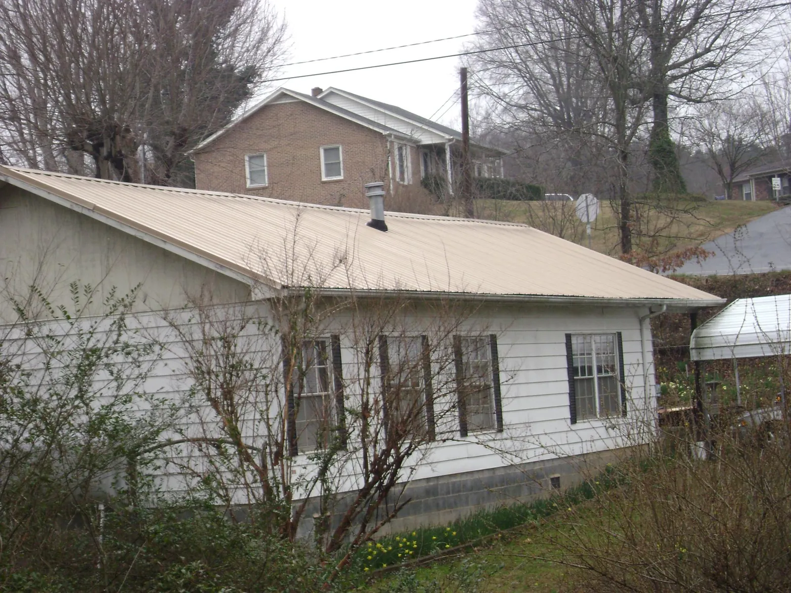 Tan metal roof on a white sided house set into a hillside — Commercial Roofing by Roofing Brothers in Faxon