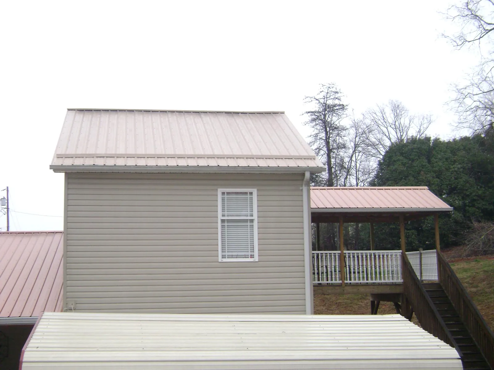 Tan metal roofs on a two story addition and attached porch, from a Roof Replacement job in Faxon